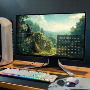 May include: A computer monitor displaying a September 2027 calendar over a landscape image of a witch hat and broom leaning against a stone wall. The setup includes a white mechanical keyboard with RGB lighting and a white computer mouse.