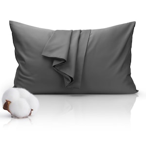 May include: A charcoal gray pillow with a folded fabric detail. A fluffy cotton boll is positioned to the left of the pillow. The pillow is rectangular and appears to be made of a smooth, soft material.