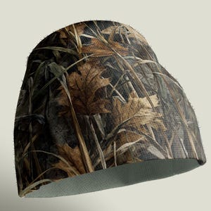 May include: A camouflage beanie hat featuring a pattern of brown leaves, green grass, and dark brown and black accents. The hat has a light green interior and is designed for outdoor activities.