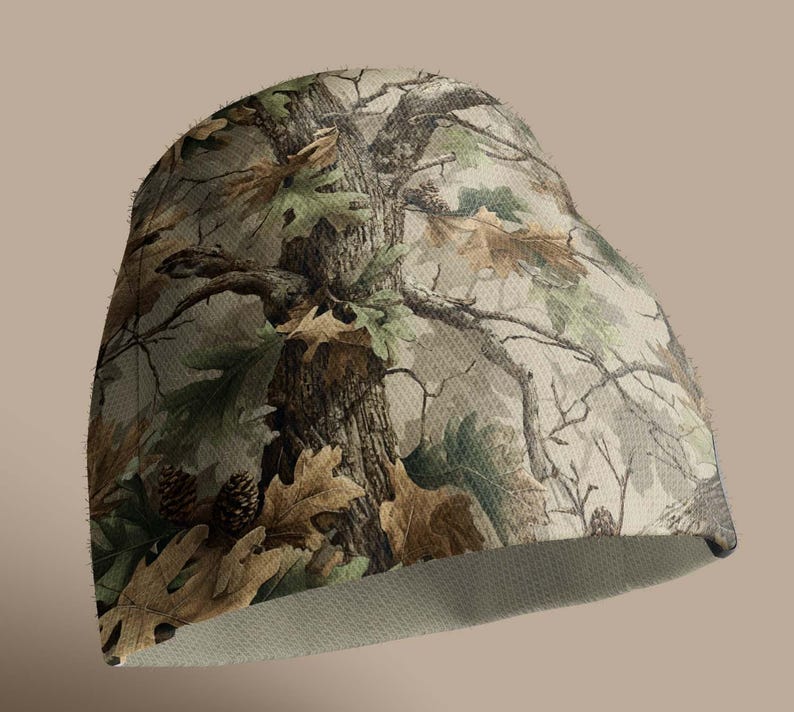 K&ouml;nnte beinhalten: Eine Camouflage-Beanie-M&uuml;tze mit einem detaillierten Waldmuster in Braun-, Gr&uuml;n- und Beiget&ouml;nen. Das Design umfasst Baumrinde, Bl&auml;tter und Tannenzapfen und erzeugt einen nat&uuml;rlichen Look. Das Innenfutter ist hellbeige.
