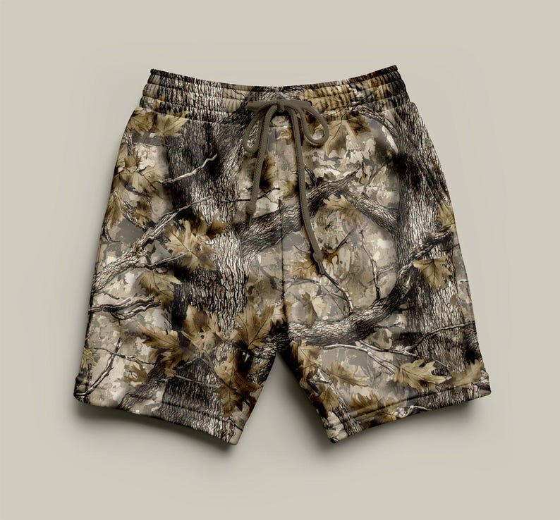 May include: Camouflage print shorts with a drawstring waist. The shorts feature a pattern of brown, tan, and grey resembling a forest scene. The shorts are made of a soft material.