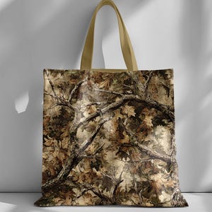 May include: A camouflage tote bag with a detailed pattern of tree branches and leaves in shades of brown, tan, and green. The bag has a beige handle and a rectangular shape, suitable for carrying various items.