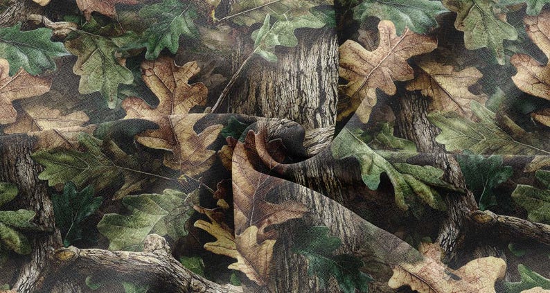 May include: Camouflage fabric with a detailed design of oak leaves and tree bark in shades of green, brown, and tan. The fabric has a realistic, textured appearance, suitable for outdoor-themed projects.