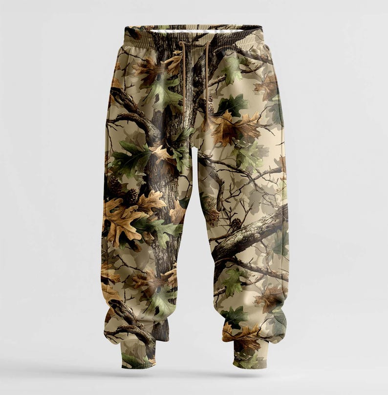 K&ouml;nnte beinhalten: Sweathose mit Camouflage-Muster, Kordelzugbund und gerippten Kn&ouml;chelb&uuml;ndchen. Die Hose zeigt einen realistischen Aufdruck von &Auml;sten, Bl&auml;ttern und Rinde in Braun-, Gr&uuml;n- und Beiget&ouml;nen. Das Gesamtdesign ahmt eine Waldumgebung nach.