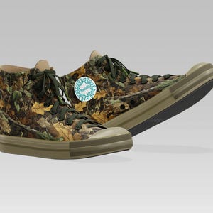 May include: High-top canvas sneakers with a camouflage pattern of brown, green, and yellow leaves. The sneakers have olive green soles, laces, and a round logo on the side. The shoes are designed for casual wear.
