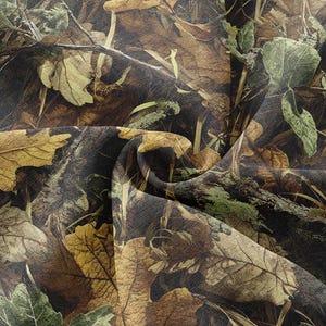 May include: Camouflage fabric featuring a detailed pattern of leaves in shades of brown, green, and yellow. The design mimics a forest floor with fallen leaves, branches, and foliage, creating a naturalistic camouflage effect.
