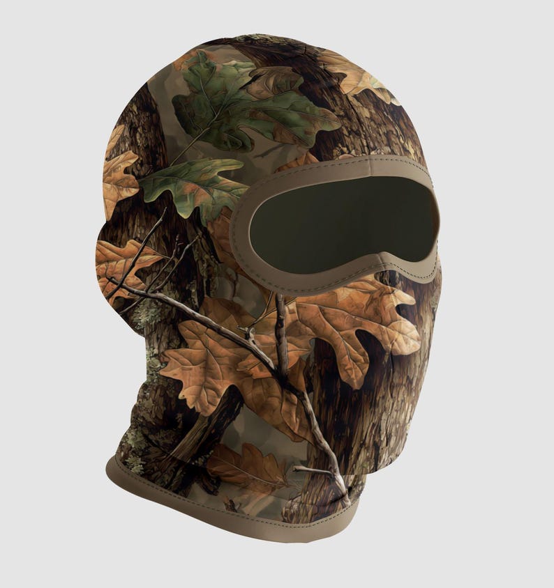 May include: A camouflage balaclava featuring a brown, green, and tan oak leaf design. The balaclava has a large eye opening and a tan trim. The fabric is printed with a realistic forest pattern, suitable for outdoor activities.