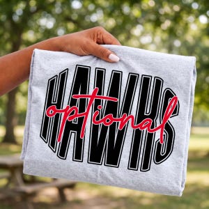 May include: A light gray t-shirt featuring the word HAWKS in large, bold black block letters with a white outline. Overlaid across the center of the black text is the word optional written in a red, cursive script font with a thin white outline.
