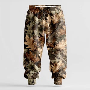 K&ouml;nnte beinhalten: Sweathose mit Camouflage-Muster und einem realistischen Eichenblatt-Design in Braun-, Beige- und Gr&uuml;nt&ouml;nen. Die Hose hat einen Kordelzug in der Taille und gerippte B&uuml;ndchen an den Kn&ouml;cheln. Der Stil ist l&auml;ssig und bequem.