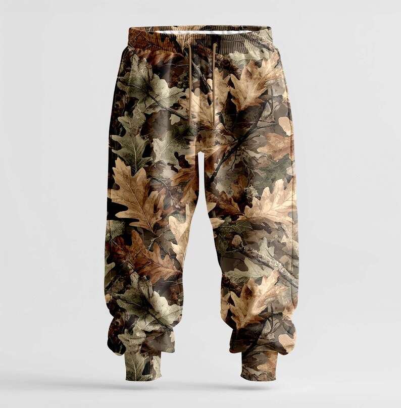 K&ouml;nnte beinhalten: Sweathose mit Camouflage-Muster und einem realistischen Eichenblatt-Design in Braun-, Beige- und Gr&uuml;nt&ouml;nen. Die Hose hat einen Kordelzug in der Taille und gerippte B&uuml;ndchen an den Kn&ouml;cheln. Der Stil ist l&auml;ssig und bequem.