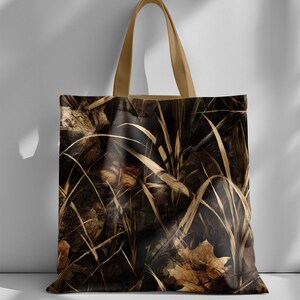 May include: A tote bag with a camouflage pattern of dried leaves and tall grass in shades of brown and tan. The bag has tan-colored handles.