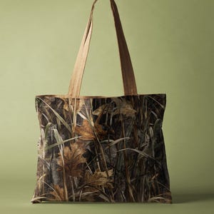 May include: A tote bag featuring a camouflage pattern of brown and tan leaves and grasses. The bag has light brown handles and a rectangular shape. The background is a solid light green.
