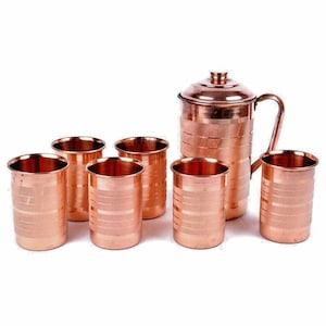 May include: A copper pitcher with a lid and handle, accompanied by six matching copper drinking glasses. Each piece has horizontal banded detailing, creating a cohesive set. The set is designed for serving beverages.