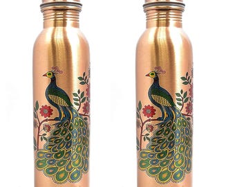 Op de afbeelding: Twee koperkleurige waterflessen met schroefdoppen. Elke fles heeft een gedetailleerd pauwenontwerp met groene, blauwe en gele veren, geplaatst op een bloeiende tak. De flessen zijn cilindrisch en lijken van metaal te zijn.