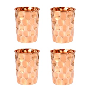 May include: Four copper-colored drinking glasses with a hammered texture. The glasses have a cylindrical shape and a shiny finish. The glasses are arranged in a square formation against a white background. The glasses are suitable for water, juice, or other beverages.