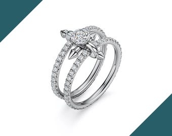 May include: A silver ring with a central diamond and two bands, one of which is encrusted with smaller diamonds. The ring features a unique design with a decorative element and pointed accents, creating a modern and elegant look.