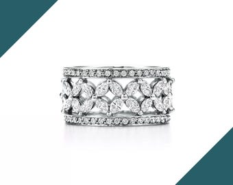 May include: A silver ring with a floral design. The ring features marquise-cut and round-cut clear gemstones. The gemstones are set in a repeating pattern around the band. The ring is set against a white background.