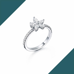 May include: A silver ring featuring a flower design. The flower is composed of six marquise-cut gemstones. The band is adorned with small, round gemstones. The ring is set against a white background.