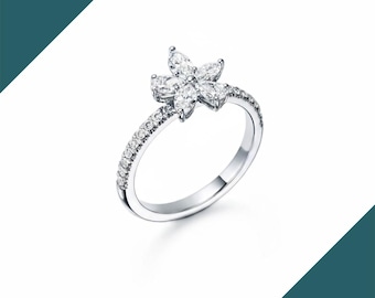 May include: A silver ring featuring a flower design. The flower is composed of six marquise-cut gemstones. The band is adorned with small, round gemstones. The ring is set against a white background.