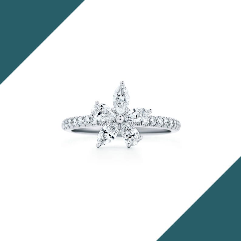 May include: A silver ring featuring a flower design made of marquise-cut diamonds. The ring's band is encrusted with small, round diamonds, creating a sparkling effect. The flower's petals are formed by six marquise-cut diamonds, with a larger diamond at the center.