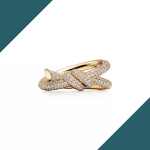 May include: A gold-colored ring with a knot design. The ring is encrusted with small, sparkling diamonds. The band of the ring is smooth and polished, while the knot portion is covered in the diamonds. The ring is set against a white background.