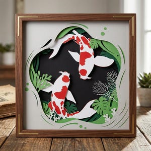May include: A framed paper art piece featuring two koi fish with red and white markings, swimming amidst green foliage. The artwork is set against a black background, framed in a brown wooden frame with gold accents. The piece is a unique home decor item.