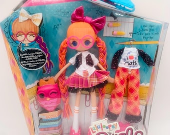 Może przedstawiać: Lalka Lalaloopsy Girls w przezroczystym plastikowym opakowaniu. Lalka ma pomarańczowe włosy, różowe okulary i szkolny mundurek. Dodatkowe ubrania i akcesoria to maska sowy, spinki do włosów i koszulka z napisem "I Math".
