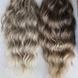 Könnte beinhalten: Zwei Bündel gewellter Haarverlängerungen. Eines ist eine Mischung aus hellbraun und blond, das andere eine Mischung aus dunkelbraun und blond. Das Haar ist in lockeren Wellen gestylt, mit einem natürlichen, verblendeten Aussehen.