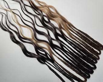 May include: A collection of wavy and dreadlock hair extensions in various shades of brown, black, and blonde. The extensions are arranged in a diagonal pattern, showcasing the different colors and textures of the hair.