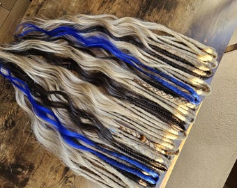 Könnte beinhalten: Eine Sammlung von Dreadlocks in verschiedenen Farben, darunter Blond, Schwarz und Blau. Die Dreadlocks sind auf einer Holzoberfläche angeordnet, um ihre Textur und ihren Stil zu zeigen. Einige Dreadlocks sind mit dekorativen Elementen verziert.