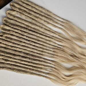 K&ouml;nnte beinhalten: Eine Ansammlung hellbrauner Dreadlocks, f&auml;cherf&ouml;rmig angeordnet. Die Dreadlocks bestehen aus einem strukturierten Material und haben an den Enden ein nat&uuml;rliches, welliges Aussehen. Der Hintergrund ist eine schlichte wei&szlig;e Oberfl&auml;che.