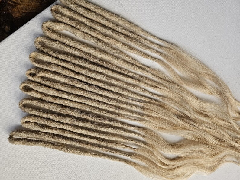 K&ouml;nnte beinhalten: Eine Ansammlung hellbrauner Dreadlocks, f&auml;cherf&ouml;rmig angeordnet. Die Dreadlocks bestehen aus einem strukturierten Material und haben an den Enden ein nat&uuml;rliches, welliges Aussehen. Der Hintergrund ist eine schlichte wei&szlig;e Oberfl&auml;che.