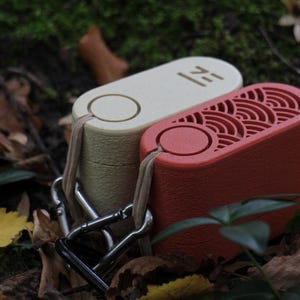 May include: Two rectangular, portable devices in cream and red, connected by a metal clasp. The cream device has the word "ZE" printed on it. The red device has a decorative, wave-like pattern. Both have a loop for attaching a lanyard.