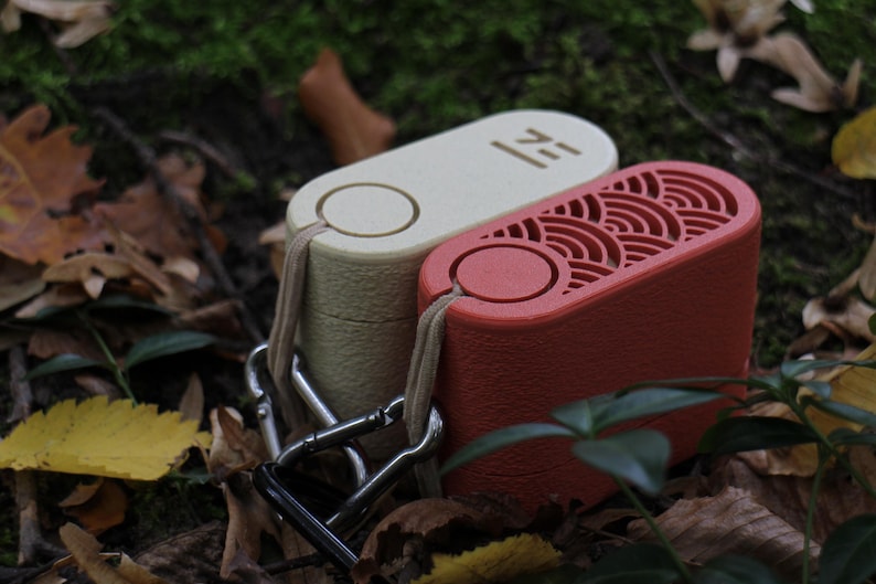 May include: Two rectangular, portable devices in cream and red, connected by a metal clasp. The cream device has the word "ZE" printed on it. The red device has a decorative, wave-like pattern. Both have a loop for attaching a lanyard.