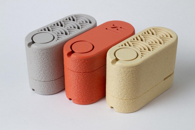 May include: Three cylindrical, textured objects in gray, orange, and beige. Each has a circular top with a small opening and a patterned vent. The objects are arranged side by side against a white background.