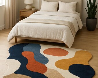 Puede incluir: Alfombra abstracta de forma orgánica con diseños en azul marino, óxido, azul claro y amarillo mostaza sobre fondo crema. La alfombra está colocada sobre un suelo de madera en un dormitorio. Dimensiones aproximadas: 180 cm x 120 cm.