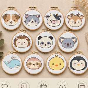 May include: Eleven circular embroidery hoops containing cross-stitch patterns of various animal faces including a dog, cat, cow, deer, hedgehog, panda, koala, whale, sloth, chick, and penguin, arranged in three rows on a light fabric background.