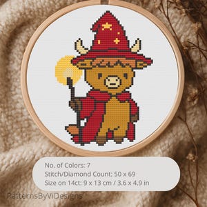 Può includere: Un ricamo a punto croce in un telaio di legno raffigura un toro dei cartoni animati con un cappello e un mantello da mago rossi, che tiene in mano un globo luminoso. Il disegno misura 9 x 13 cm e ha 7 colori. Il testo "PatternsByViDesigns" è in basso.