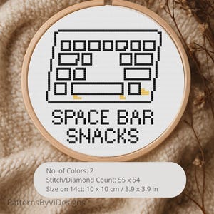 May include: A cross-stitch design in a wooden hoop features a black and white keyboard layout with the text "SPACE BAR SNACKS." The design is 3.9 x 3.9 inches and uses two colors. The background is a neutral beige.