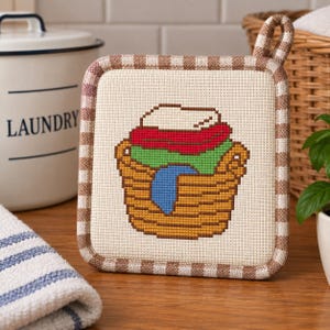 Peut inclure: Un dessous de plat carré avec un centre en tissu crème orné d'un motif au point de croix représentant un panier à linge en osier brun rempli de vêtements rouges, verts et bleus, bordé d'un tissu à carreaux bruns et blancs avec une boucle.