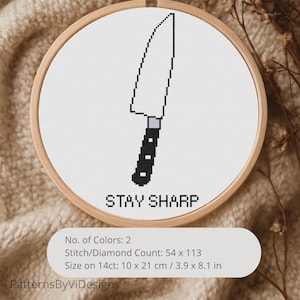 Puede incluir: Bordado de punto de cruz en un aro de madera con un diseño de cuchillo en blanco y negro y el texto "STAY SHARP". El diseño está sobre tela blanca. El aro mide 10 x 21 cm.