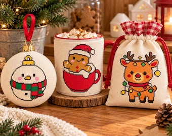 Può includere: Una pallina di Natale bianca rotonda con un pupazzo di neve a punto croce, una tazza in ceramica bianca con un omino di pan di zenzero a punto croce in una tazza rossa e un piccolo sacchetto con coulisse color crema con un disegno di renna a punto croce.