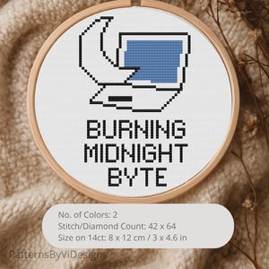 May include: Cross-stitch embroidery in a wooden hoop featuring a pixelated computer design with a blue screen. The text "BURNING MIDNIGHT BYTE" is below the image. The design is 3 x 4.6 inches on 14ct fabric.