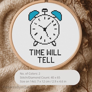 May include: A cross-stitch embroidery in a wooden hoop features a pixelated clock design with blue accents and the words "TIME WILL TELL." The embroidery measures 2.9 x 4.6 inches and is set against a neutral background.