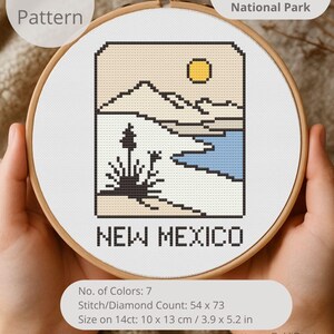 May include: A cross-stitch pattern in a wooden hoop featuring a landscape design of New Mexico's White Sands National Park. The design includes mountains, a lake, and a sun. The text "NEW MEXICO" is at the bottom. The pattern size is 3.9 x 5.2 inches.