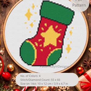 May include: A cross-stitch pattern of a Christmas stocking in a wooden embroidery hoop. The stocking is red with green accents and a yellow star. The pattern size is 3.9 x 4.7 inches. The PDF pattern is available.