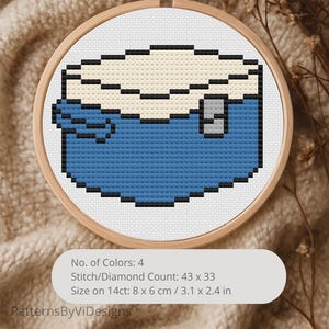 Puede incluir: Un diseño de punto de cruz de una caja azul y crema, enmarcado en un aro de madera. El diseño está pixelado, con un contorno negro. El texto "No. of Colors: 4, Stitch/Diamond Count: 43 x 33, Size on 14ct: 8 x 6 cm" es visible.