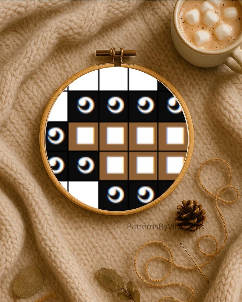 May include: A cross-stitch embroidery hoop with a geometric pattern in black, white, and brown. The design features squares and eye-like shapes. The hoop is set on a beige knitted surface, with a cup of coffee and a pinecone nearby.
