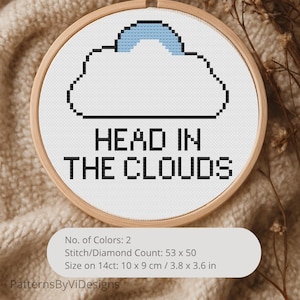 May include: A cross-stitch embroidery hoop featuring a pixelated cloud design with a blue top and the words "HEAD IN THE CLOUDS" in black. The embroidery is set in a wooden hoop, with a size of 3.8 x 3.6 inches.