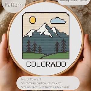 May include: Cross-stitch pattern of the Colorado Rocky Mountains in a wooden embroidery hoop. The design features a mountain range, trees, a sun, and a cloud. The word "COLORADO" is stitched at the bottom. The pattern size is 4.6 x 5.4 inches.
